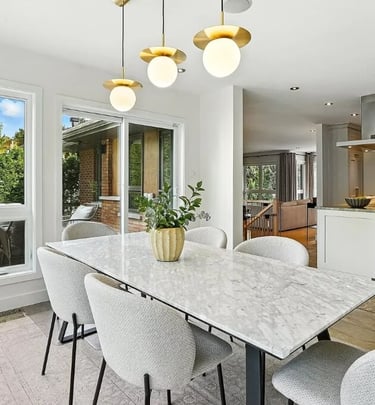 Dining area with a marble table, upholstered chairs, and an open kitchen in the background.