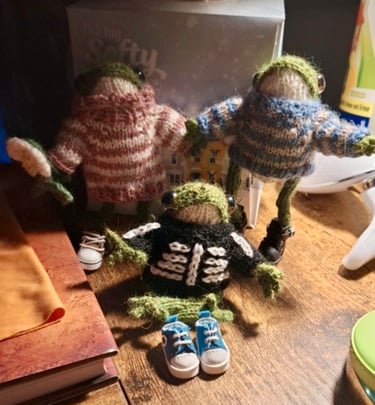 a group of knitted little froggies in jumpers sitting on a table