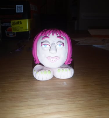 Handmade clay sculpture of a character head with pink hair and two large feet.