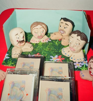 Handmade clay figurines of cartoon faces on feet displayed with cassette tapes on a red surface.