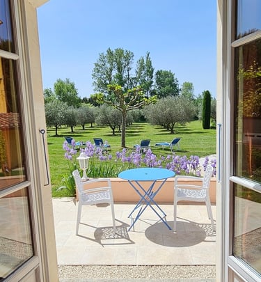 porte fenêtre ouverte du salon des hôtes vue sur jardin, iris en fleur et chaise, table ronde bleu