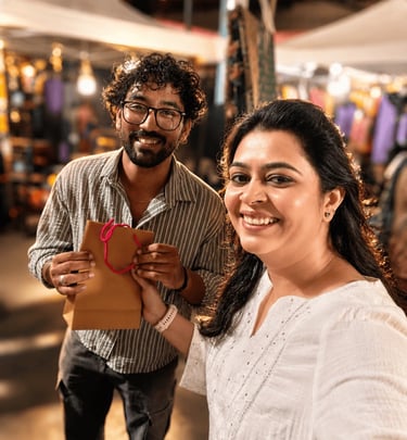 Two smiling women displaying artisanal perfumes and essential oils at an outdoor night market stall.