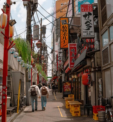 Crowded narrow alley in Tokyo's Shinjuku district featuring colorful restaurant signs and traditional lanterns.