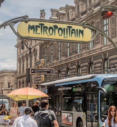Classic Art Nouveau Metropolitain subway sign above a busy Paris street with a blue electric bus and pedestrians.