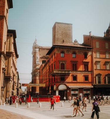 Crowded public square in Bologna, Italy, with red brick buildings and a medieval stone tower.