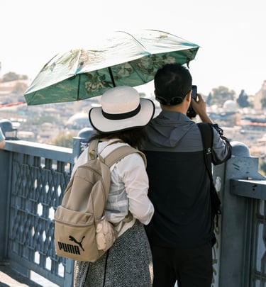 A couple with a sun umbrella and backpack sightseeing and taking photos from a bridge in Istanbul.