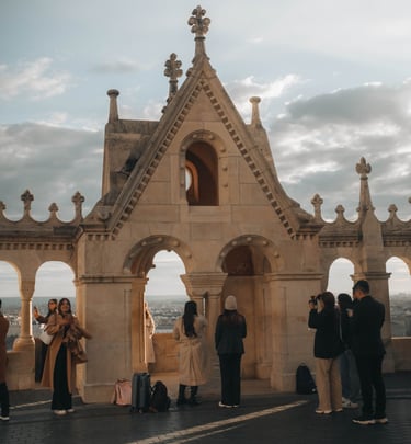 Tourists taking photos at the Fisherman's Bastion stone lookout in Budapest, Hungary at sunset.