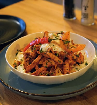 Spicy chicken strips served over creamy yogurt sauce with red peppers and fresh herbs in a white bowl.
