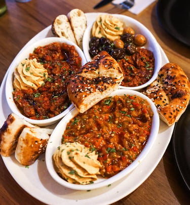 A Middle Eastern appetizer platter with hummus, shakshuka, olives, and warm pita bread on a wooden table.