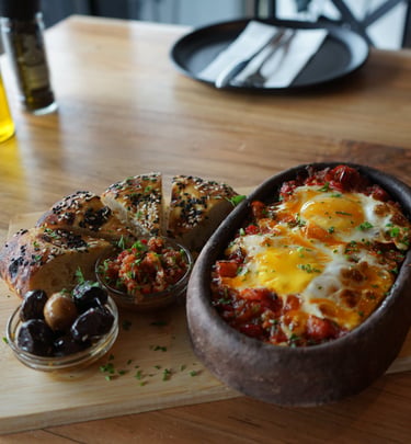 Authentic shakshuka with baked eggs in a stone bowl served with pita bread and olives on a wooden board.