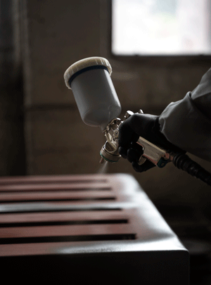 A gloved worker uses a professional spray gun to apply a fine paint finish to a metal surface.