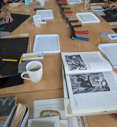 a linocut workshop with all the printmaking tools out on the desk and cups of tea and coffee