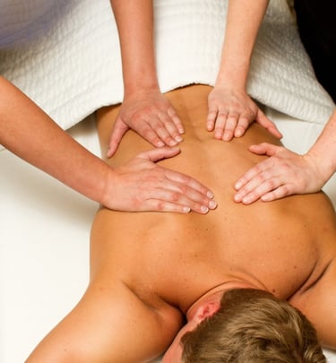 Masaje a cuatro manos realizado por dos terapeutas profesionales sobre la espalda de un hombre