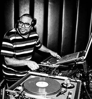 DJ Rico Sanchez wearing headphones mixing vinyl records on turntables in a club setting