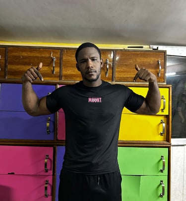 A fit man in a black Mountfit workout shirt posing in front of colorful gym lockers.