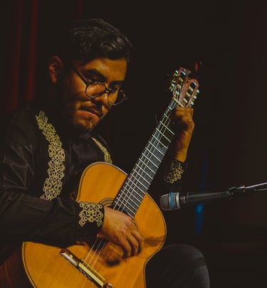 Classical guitarist in an embroidered shirt performing a solo acoustic set on stage.