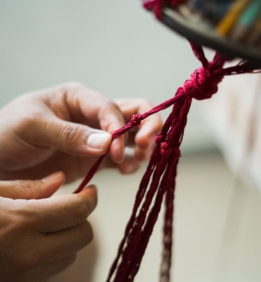 Artesana realizando nudos decorativos de macramé con cordón rojo hechos a mano.