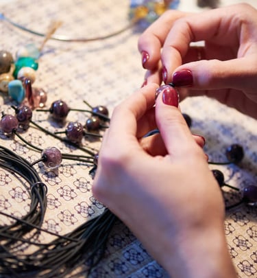 Artesana joyera creando collares de joyería artesanal con cuentas de vidrio moradas y cordones negro