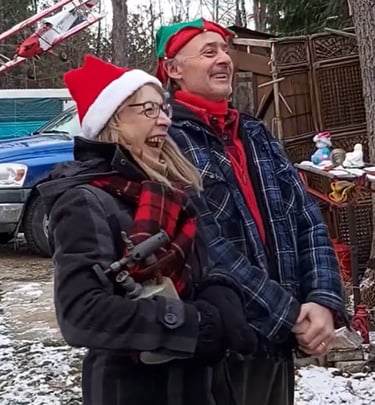 Hank & Stells wearing Christmas hats celebrates outdoors in a snowy yard with holiday decorations.