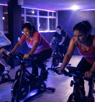 grupo de mujeres en una clase de spinning en interiores oscuros con iluminación de neón violeta