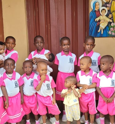 Group of African schoolchildren in pink uniforms posing together outside near a religious painting.