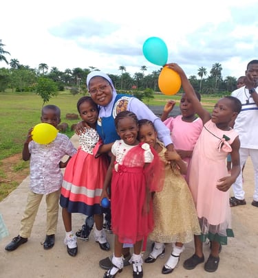 Smiling group of young children and a nun holding colorful balloons at an outdoor charity event.