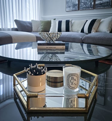 elegant, mirrored, circular coffee table with a tray, books and candles, set against a sofa backdrop