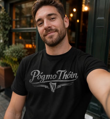 A man smiling outdoors while wearing a black Póg mo Thóin graphic t-shirt with a celtic harp.