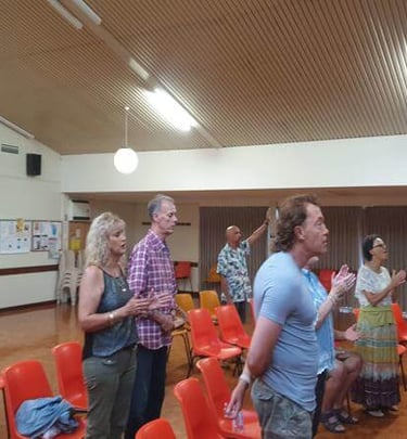 Congregation engaged in worship with hands raised inside the church hall.