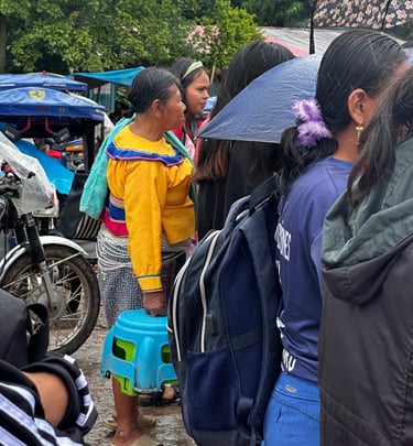 Indigenous woman in traditional yellow clothing waiting in line at an outdoor market in the rain.