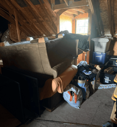 An attic with a bunch of junk: couch, chair, garbage bags