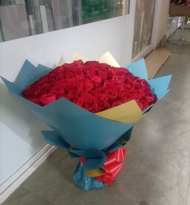 A large bouquet of fresh red roses wrapped in blue and gold paper with a red ribbon.