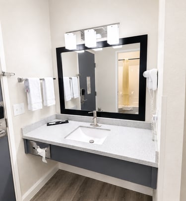 Modern hotel bathroom vanity with granite countertop, square sink, and black framed mirror.
