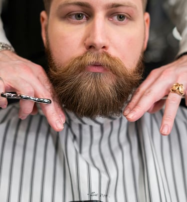 Barbero profesional recortando la barba roja y abundante de un hombre con tijeras