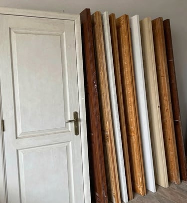 A collection of reclaimed wooden interior doors in various finishes leaning against a white wall.