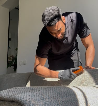 a man in a black shirt and gloves is cleaning a couch