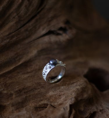 Handcrafted sterling silver ring with a dark pearl set on textured rustic wood.