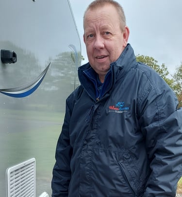 William Wilson in a Wilson Caravan Towing jacket standing next to a silver caravan outdoors.