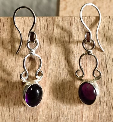 Handmade sterling silver drop earrings with oval purple amethyst gemstones on a wooden background.