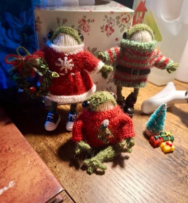 a group of knitted frog ornaments in Christmas outfits