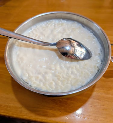 A metal bowl of creamy homemade rice pudding with a spoon on a wooden table.