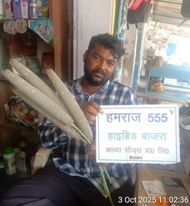 Indian farmer holding Hamraj 555 hybrid bajra millet crops and a product sign in a rural shop.