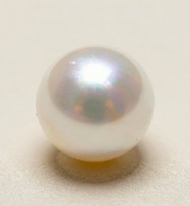 Macro photography of the sharp, bright reflection on a white pearl, demonstrating superior lustre. The background is a soft Ivory Cream.