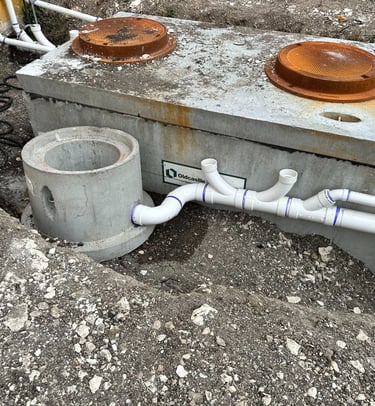 Underground concrete septic tank installation with PVC piping and riser access covers.