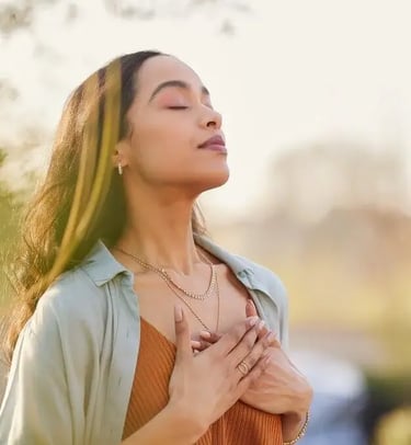 Une femme respire profondément en se tenant debout à l'extérieur, savourant un moment de sérénité et de connexion.