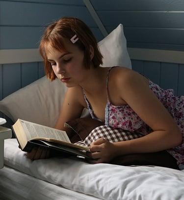 Una mujer con un vestido rosa está leyendo un libro acostada en una cama