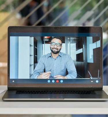A laptop screen showing a video call with a man in a business shirt holding a pen
