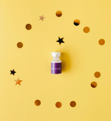 pequeño frasco de vacuna médica con etiqueta morada rodeado de confeti dorado