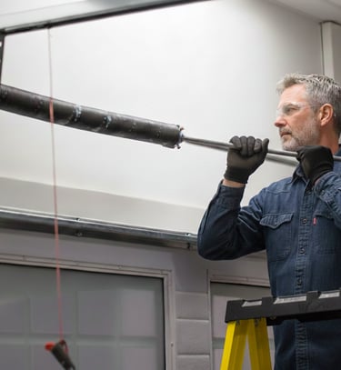 A technician on a ladder performing a professional garage door spring repair and replacement.