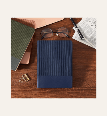 picture of leather-bound journals in dark blue and olive green on a table & showing reading glasses